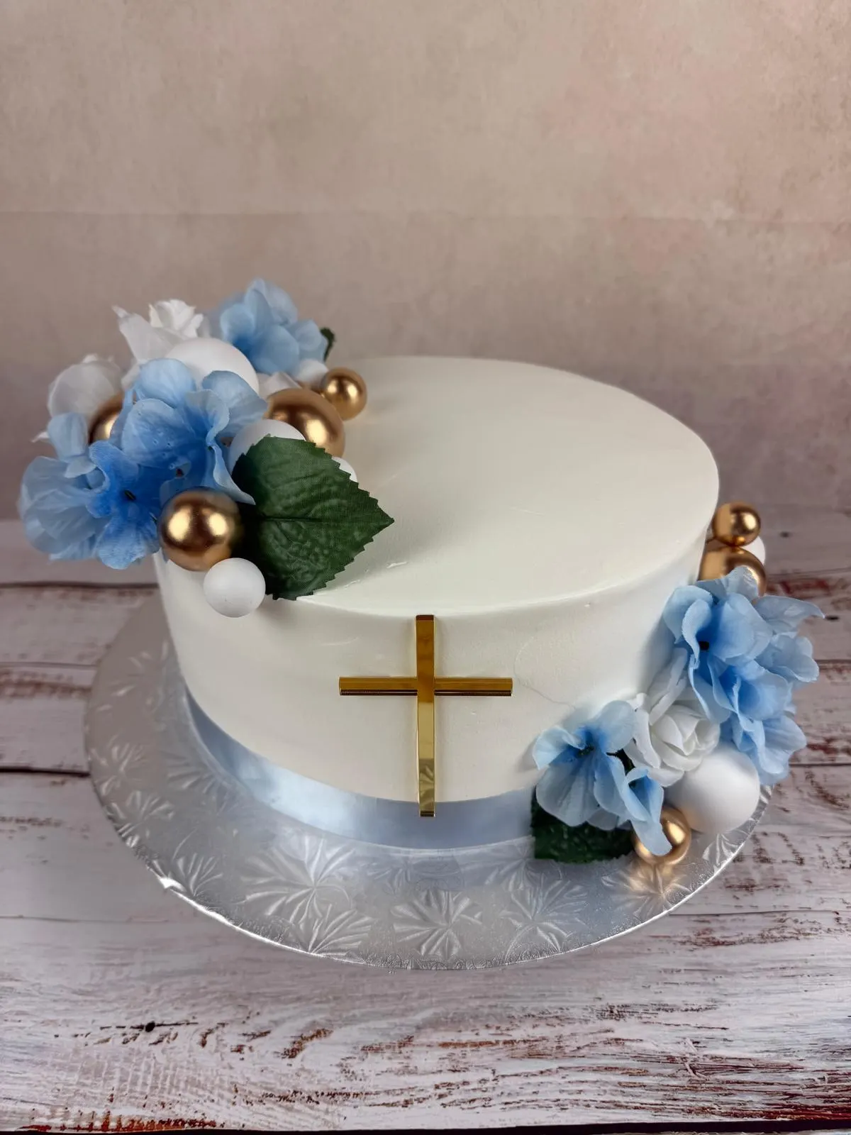 White baptism cake with blue flowers and a gold cross