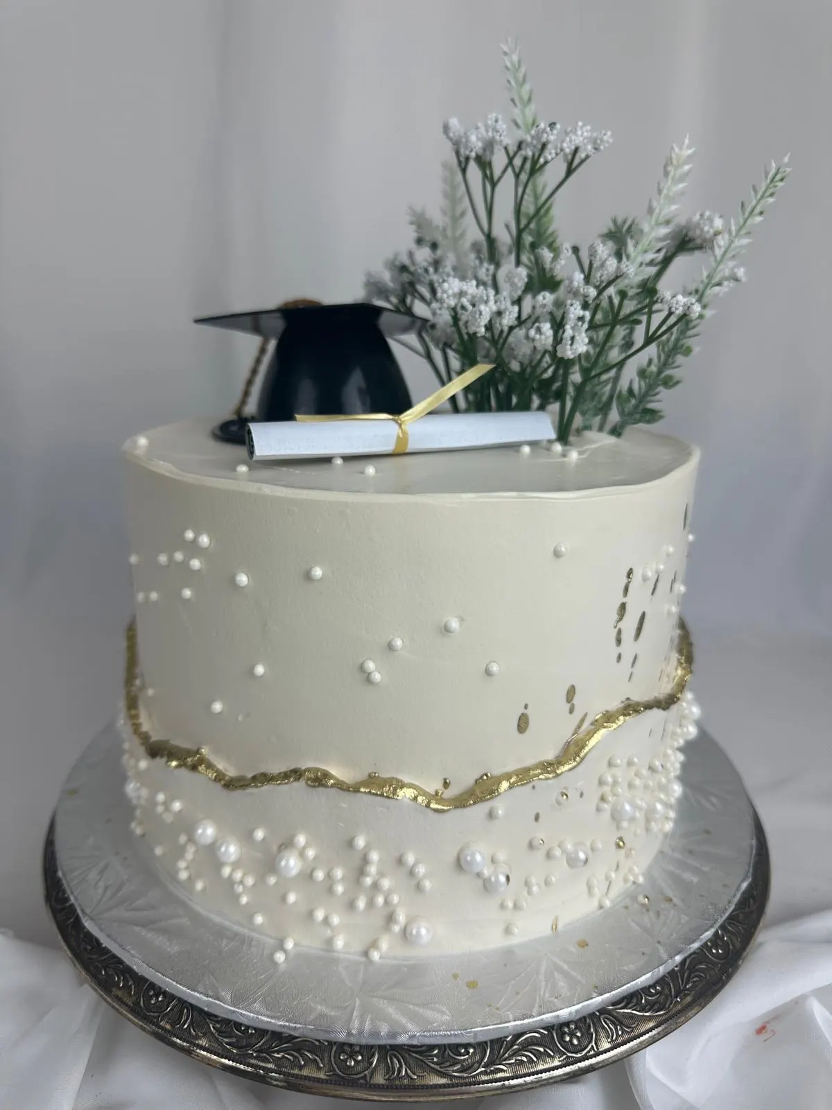 White graduation cake with pearls, a gold seam and a graduation cap